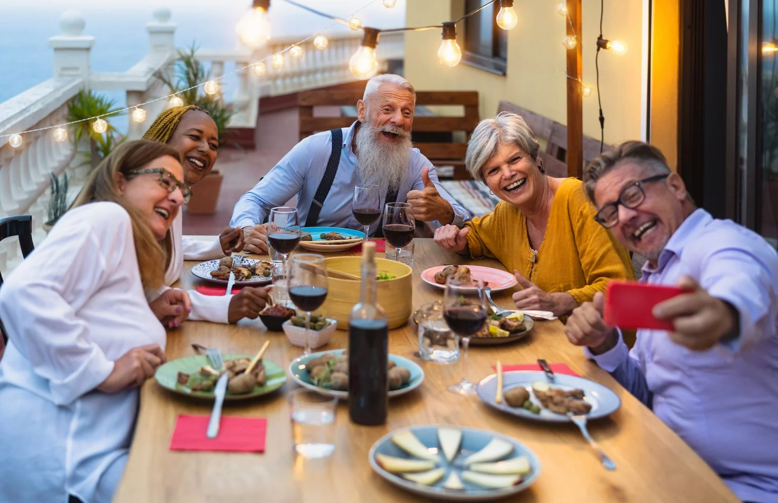 senior friends having fun dining together while taking selfie with mobile smartphone on house patio