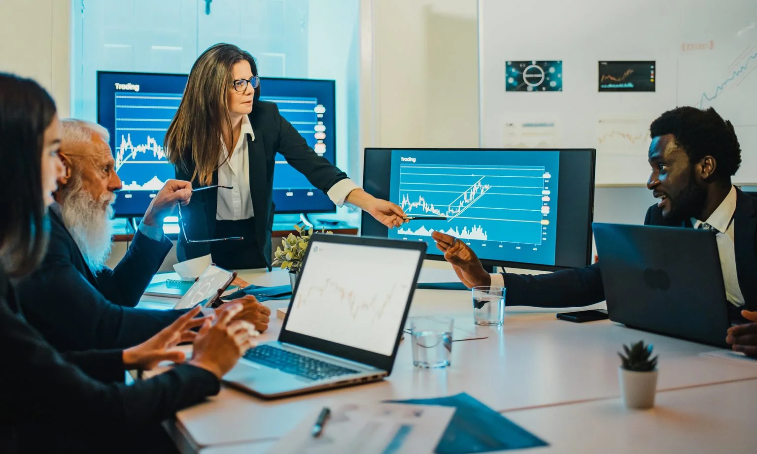 Businesswoman presenting stock market screens to her colleagues in a modern office