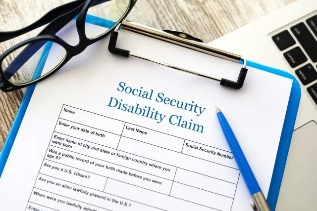 Disability claim form on a clipboard next to a pair of glasses