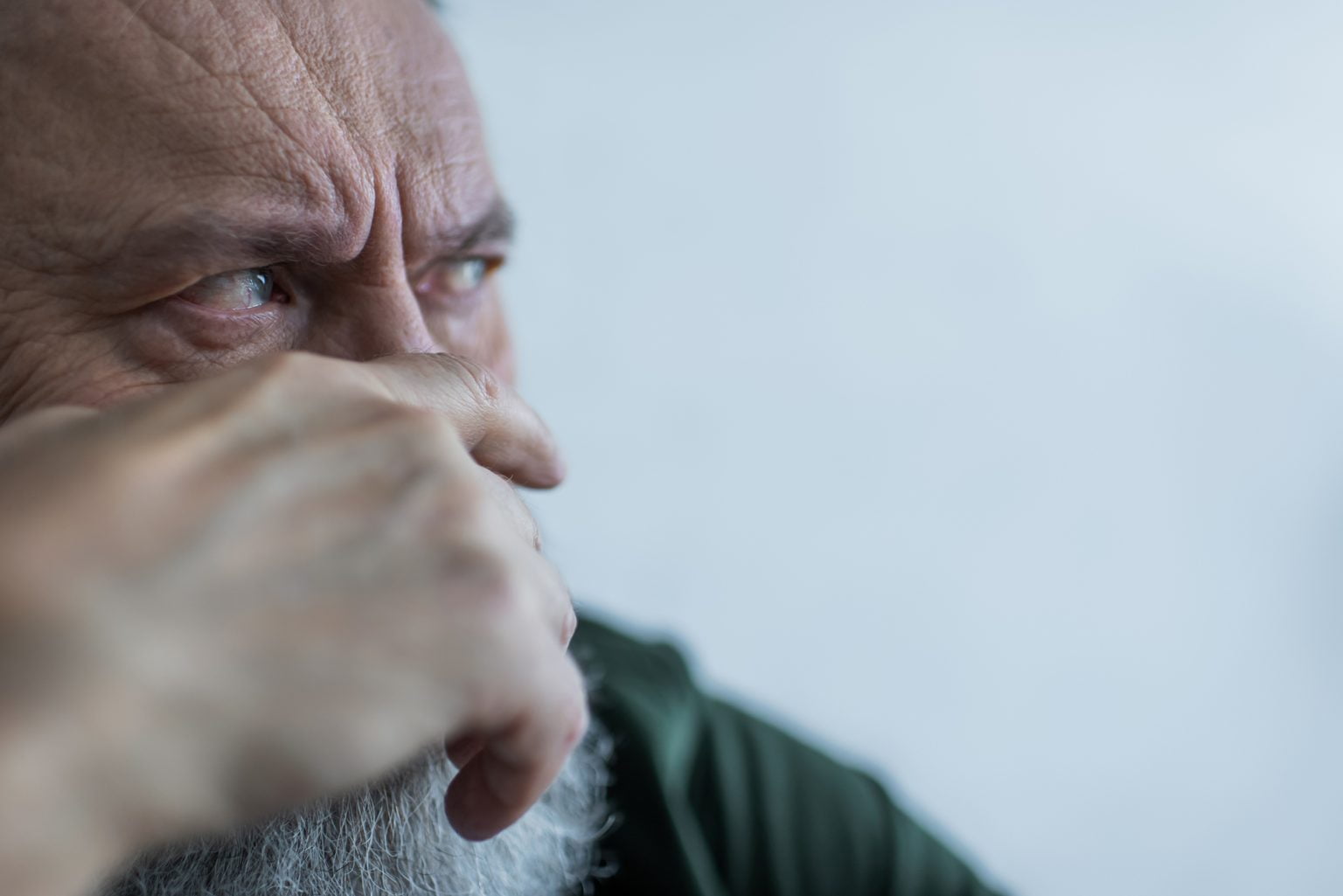 portrait of displeased senior man with beard frowning while looking away and covering face with hand