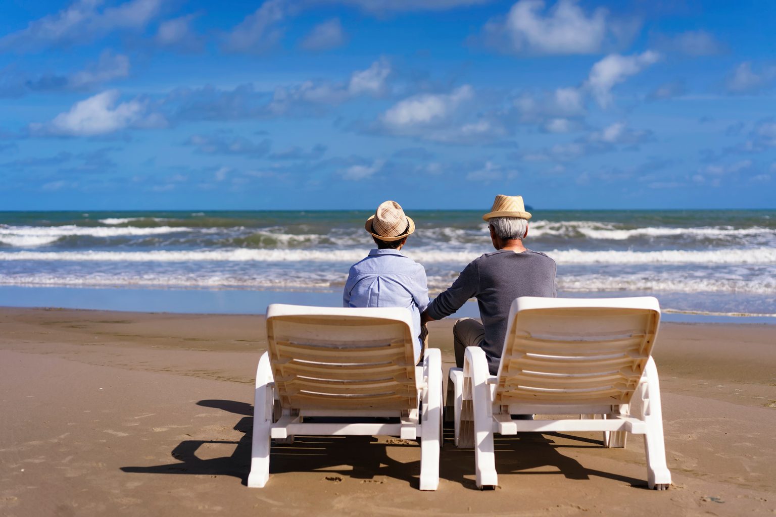 Senior couple sitting on chairs on the beach and looking at the ocean