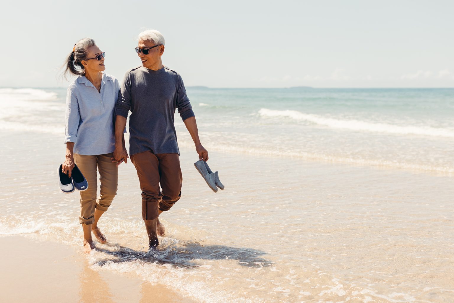 Senior couple strolling happily along the beach in the sunshine