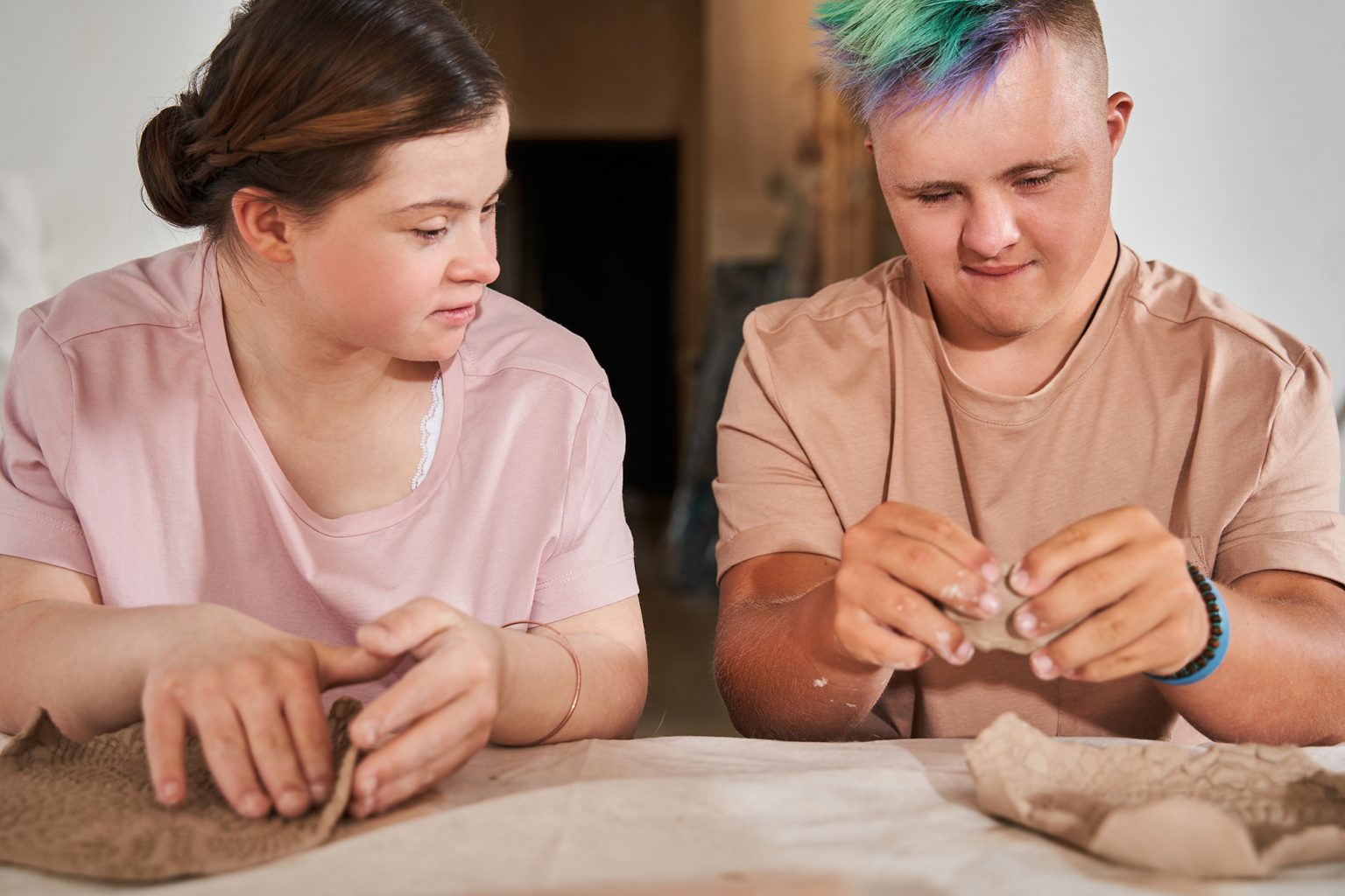 Teens with down syndrome looking at the each other while making dishes from clay