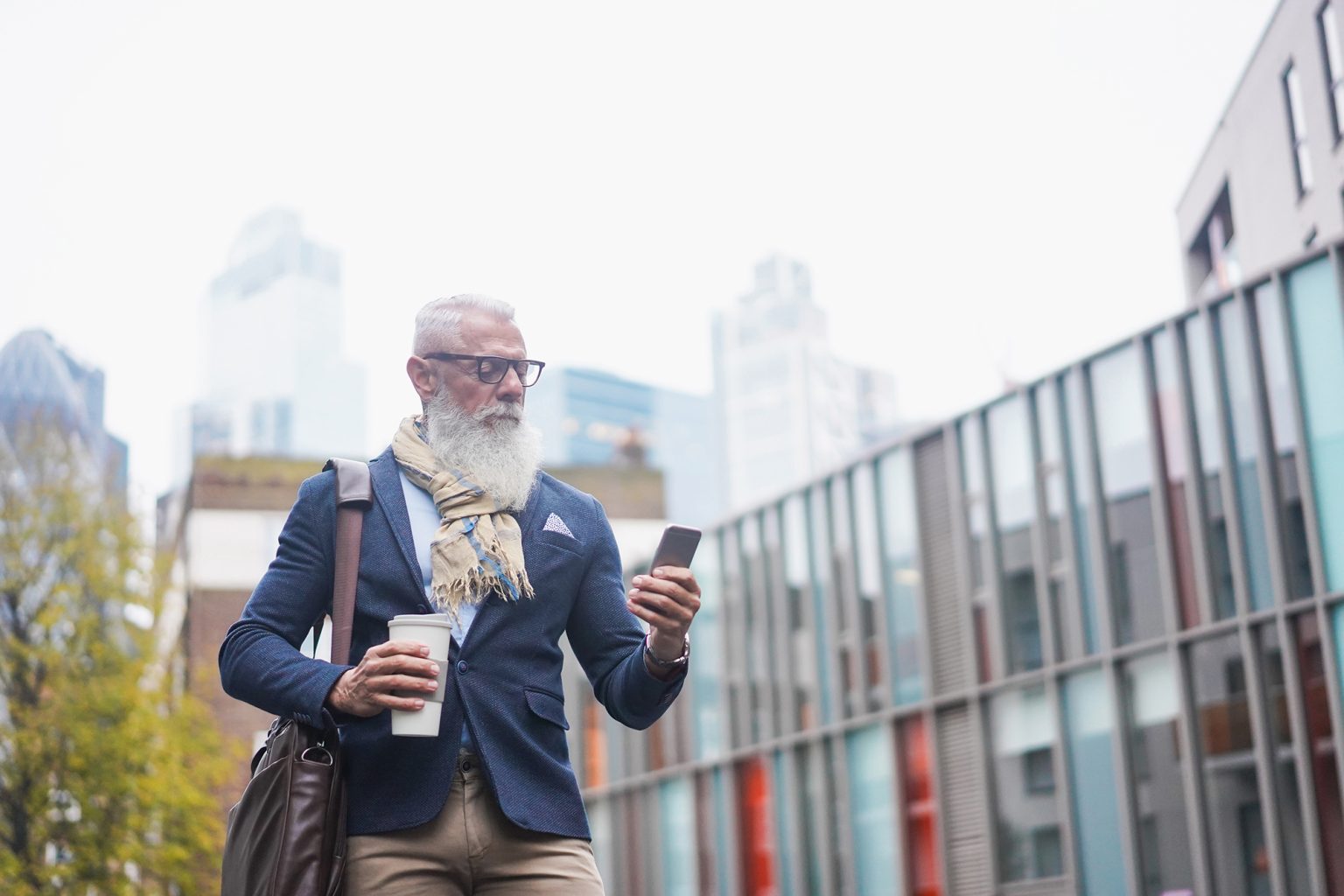 Senior man looking at phone and holding coffee with a city landscape in background