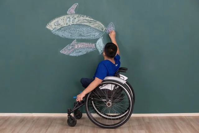 young boy in wheelchair coloring in fish on a chalkboard