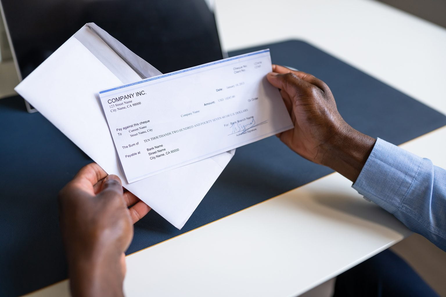 Close up of hands holding a paycheck and envelope at a desk