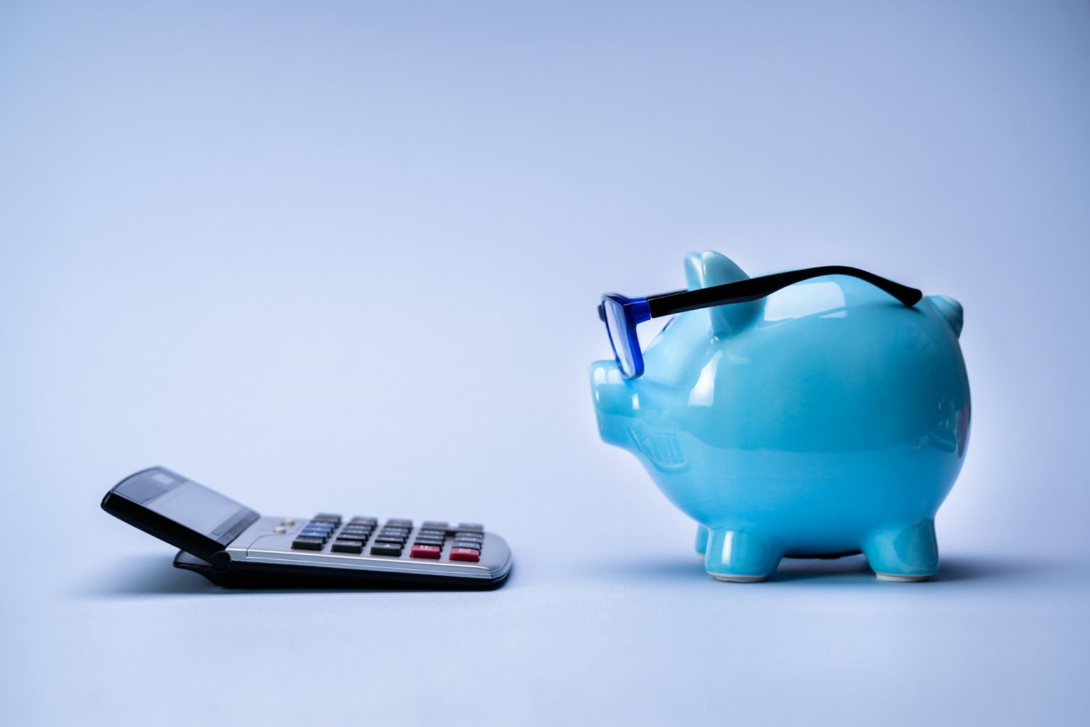 Piggy bank wearing eye glasses facing a calculator on a blue background