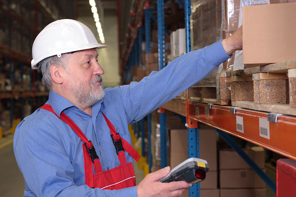 Older A worker with scanner in a factory maintaining stocks of finished products on the shelves in a storeroom.