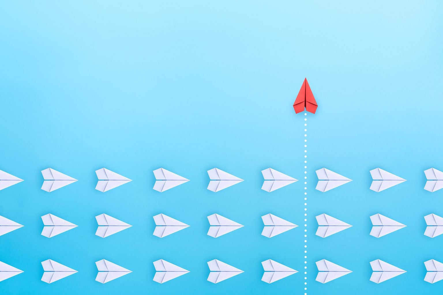 Group of white paper plane in one direction and one red paper plane pointing in different way on blue background