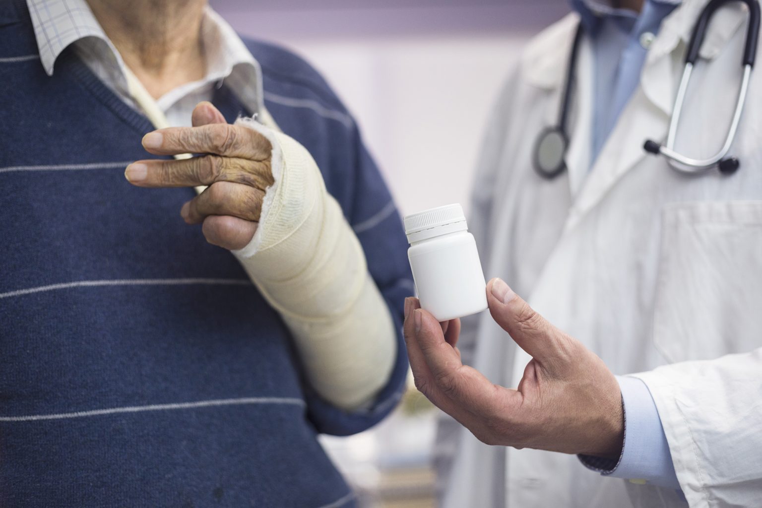 Close up of an arm in a cast next to a doctor holding a bottle of pills