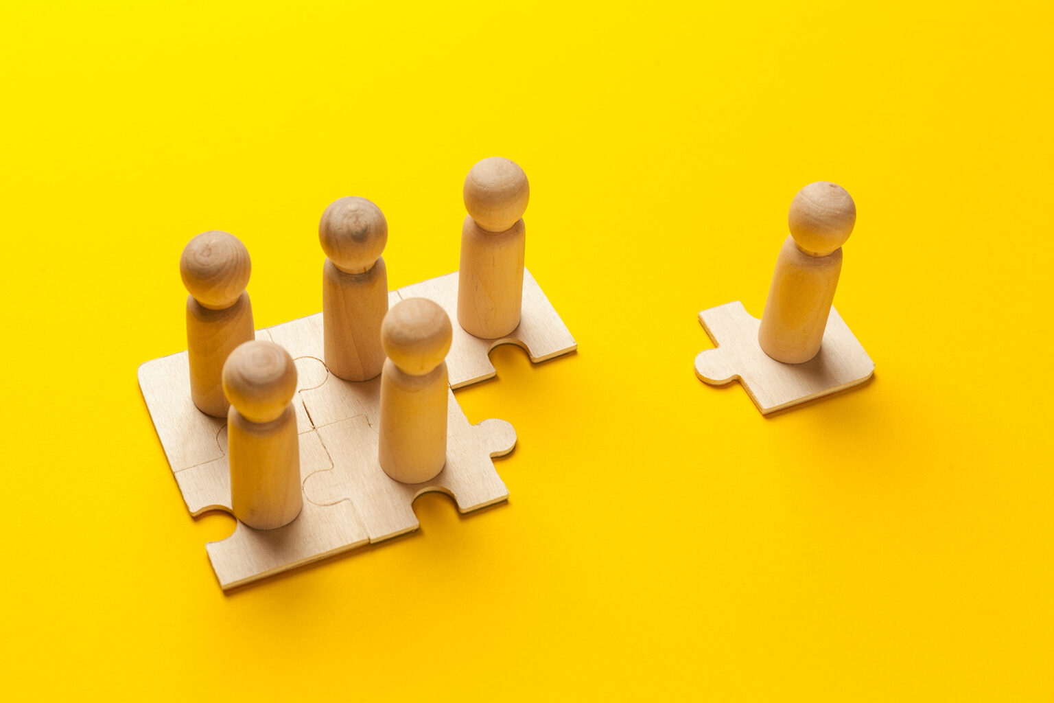 Wooden figures on puzzle pieces on yellow background
