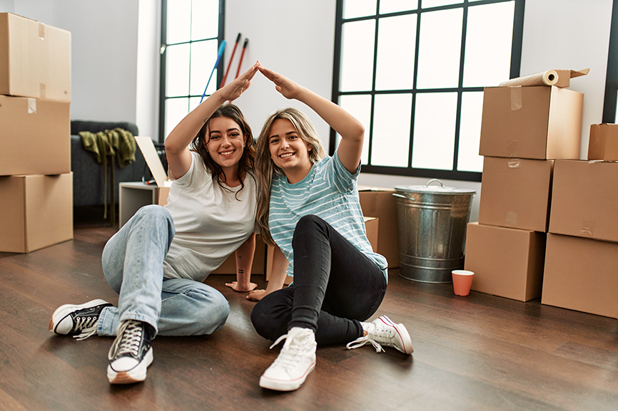 Young couple doing house symbol with arms raised at new home