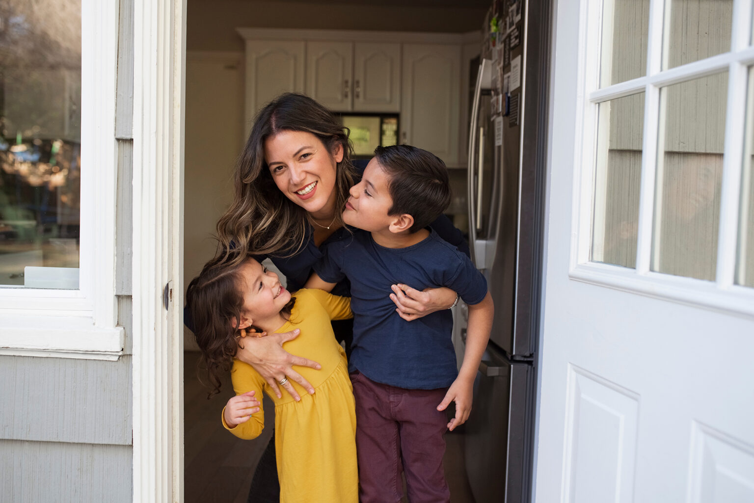 Portrait of smiling mother embracing children while standing at doorway