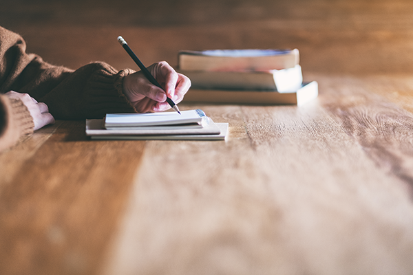 Closeup image of a woman writing on blank notebook on wooden table