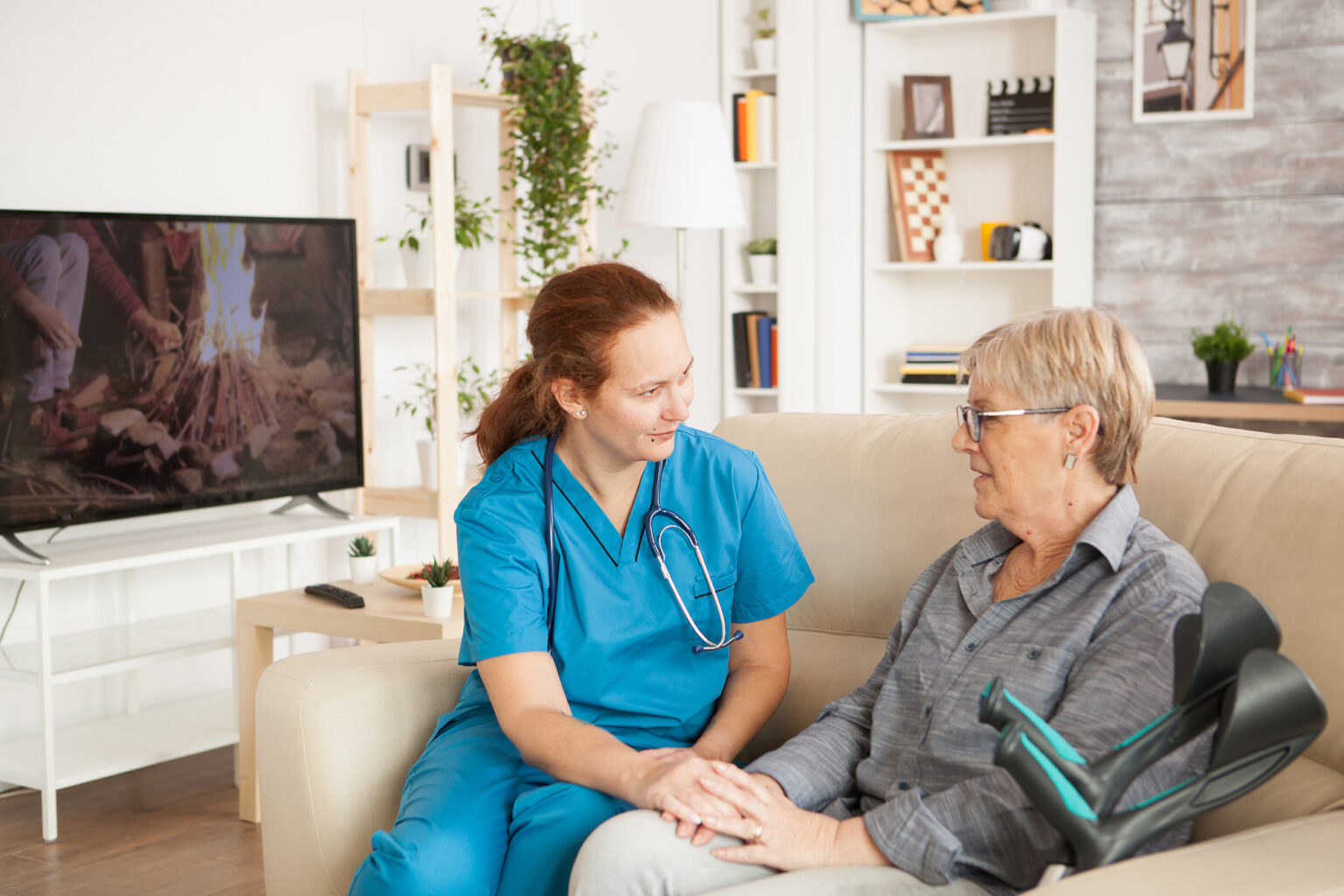 Female nurse sitting on a couch with a senior women with crutches