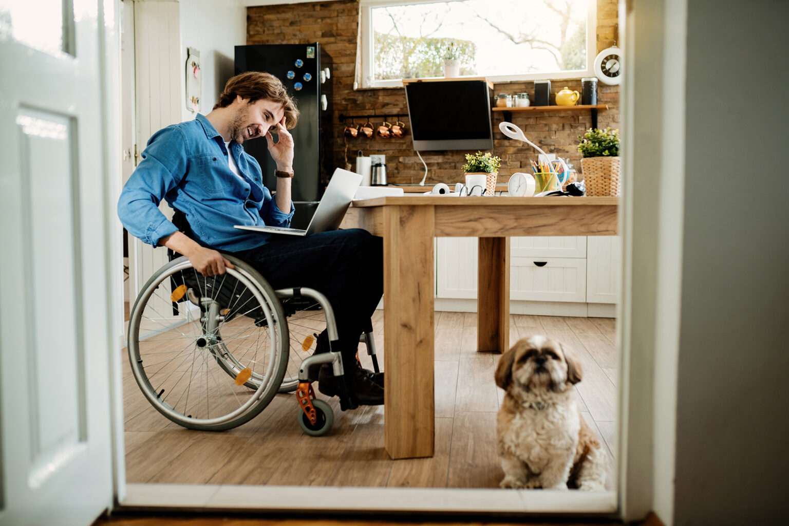 Happy disabled freelance worker using laptop while being with his dog at home