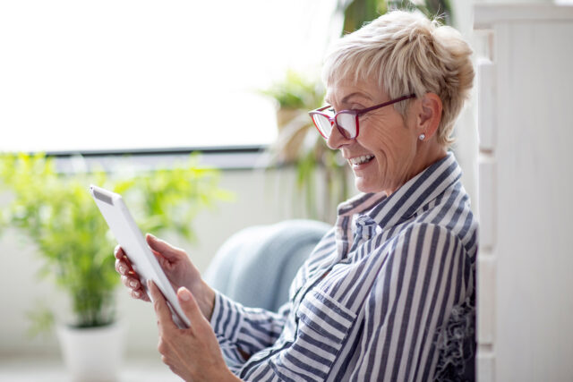 Old good looking woman sitting and use tablet to comunicate with