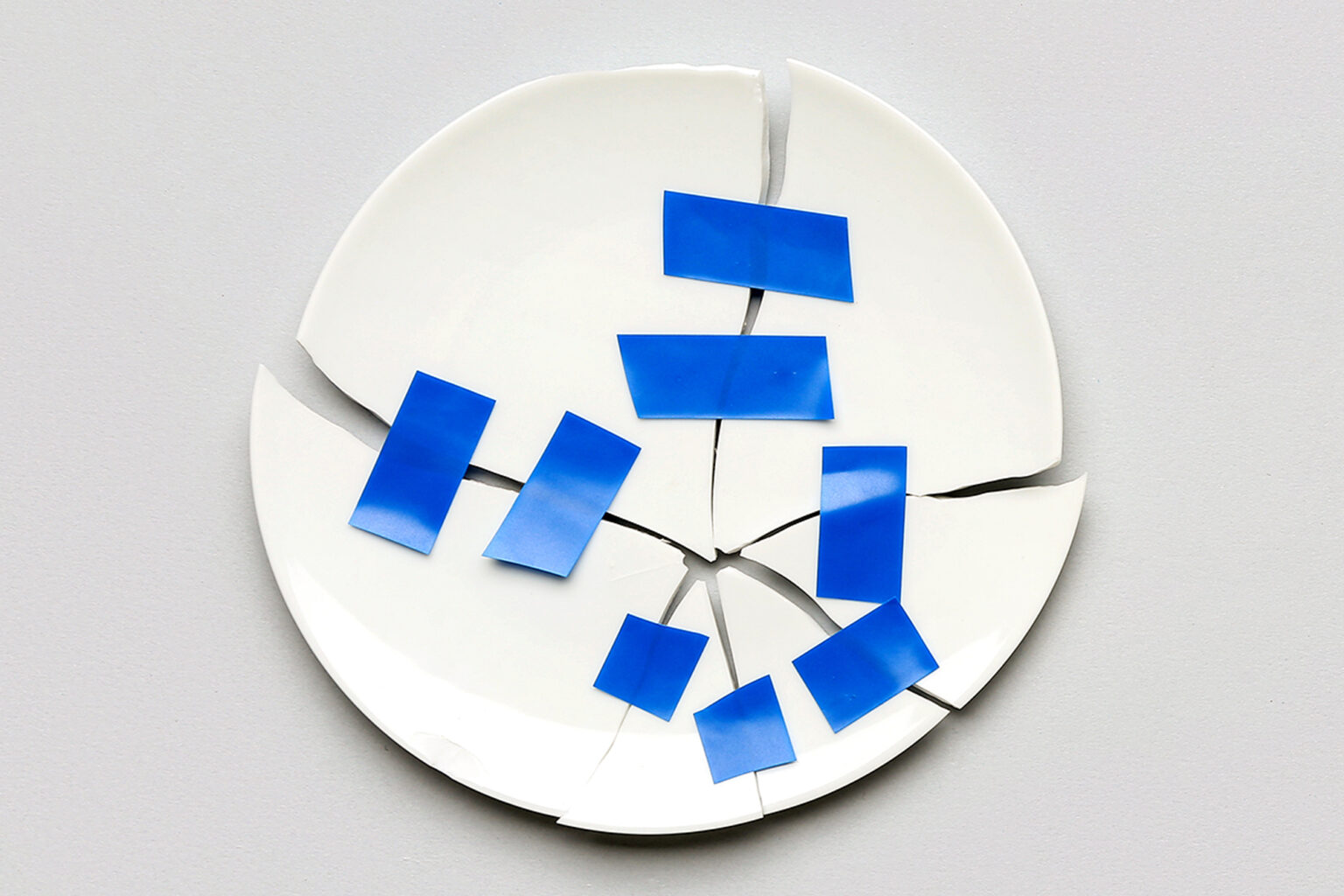 Broken plate with adhesive tape on light background