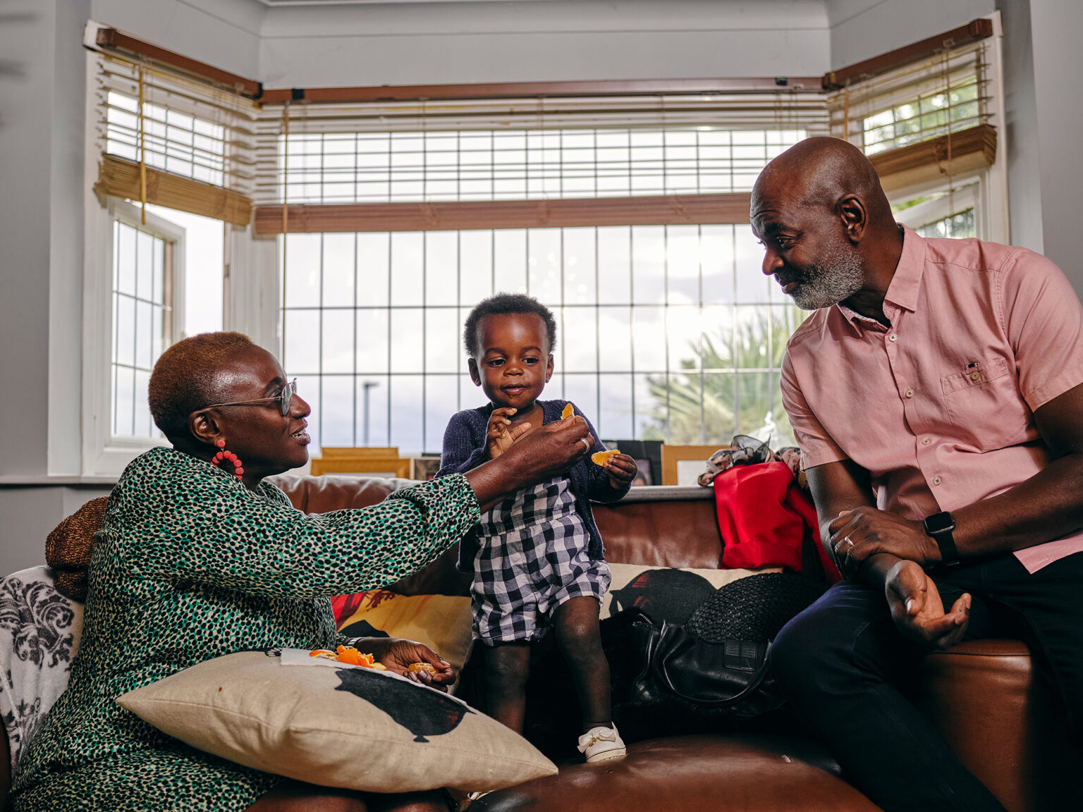 Grandparents giving food to granddaughter on a leather couch