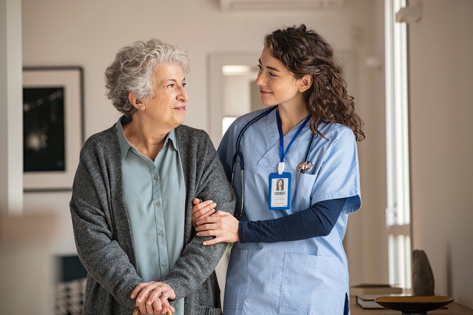 Caregiver assists senior woman walking in home