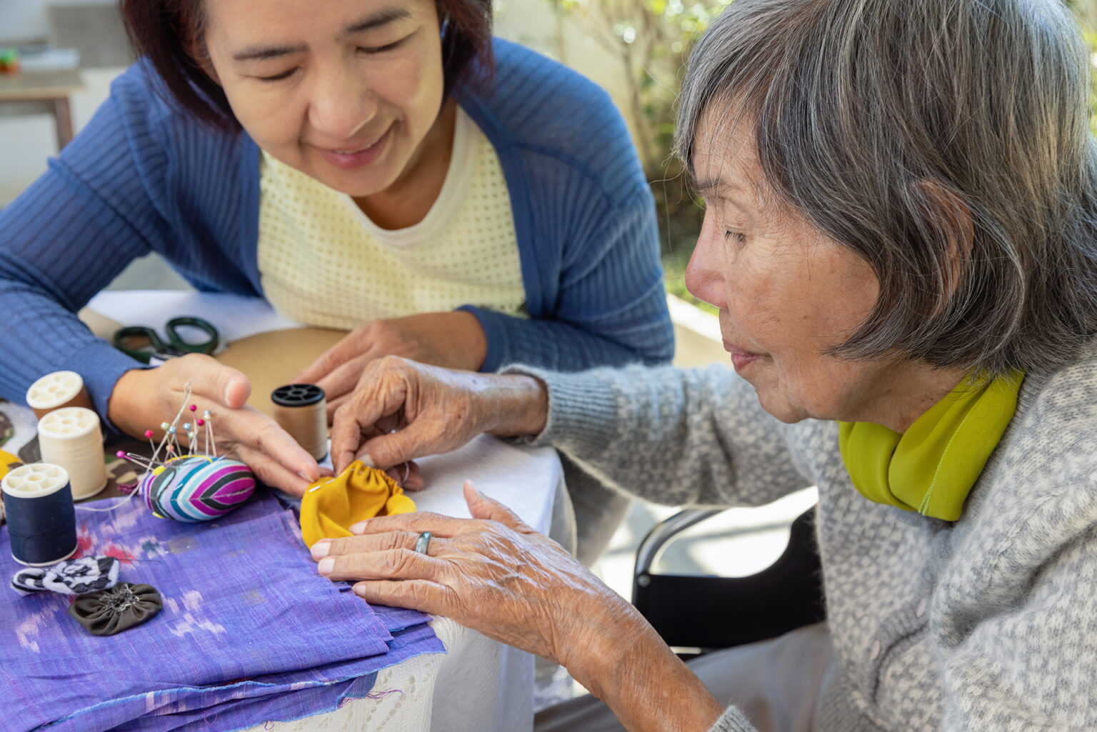 Daughter helping elderly mother with needlepoint