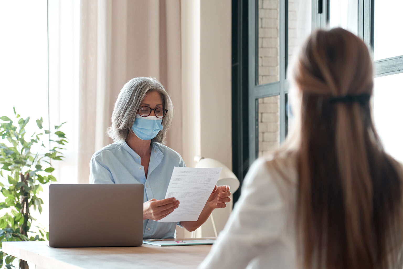 Senior employer wearing face mask reading seeker employment application