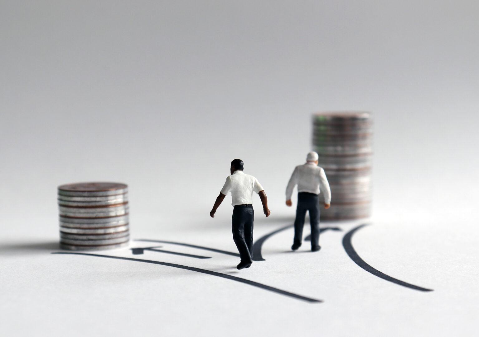 Two miniature men walking toward a stack of coins of different heights