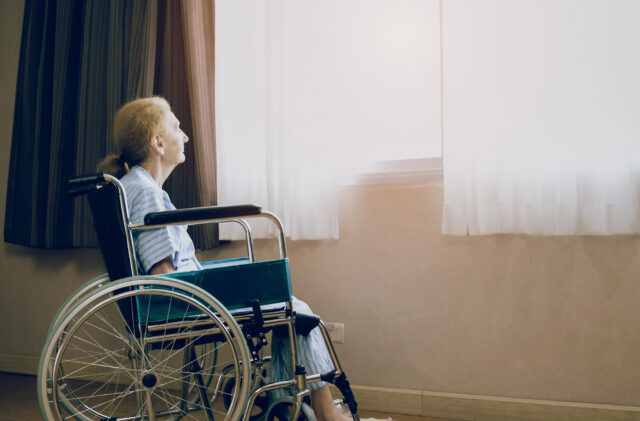 elderly woman in wheelchair while looking out the window in nursing home