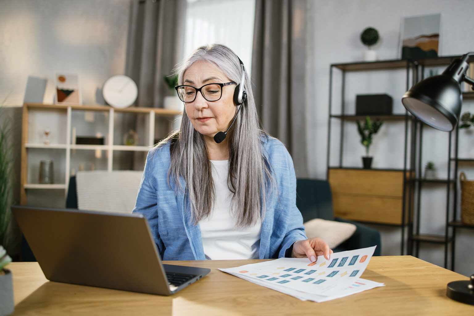 Cheerful mature woman presenting financial report to colleagues through video call on laptop