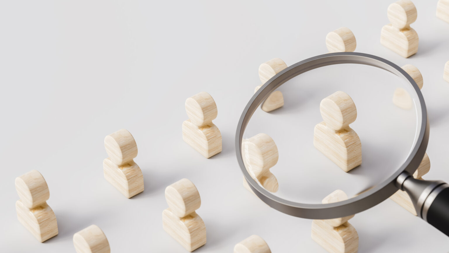 Magnifying glass over wooden people on a gray background