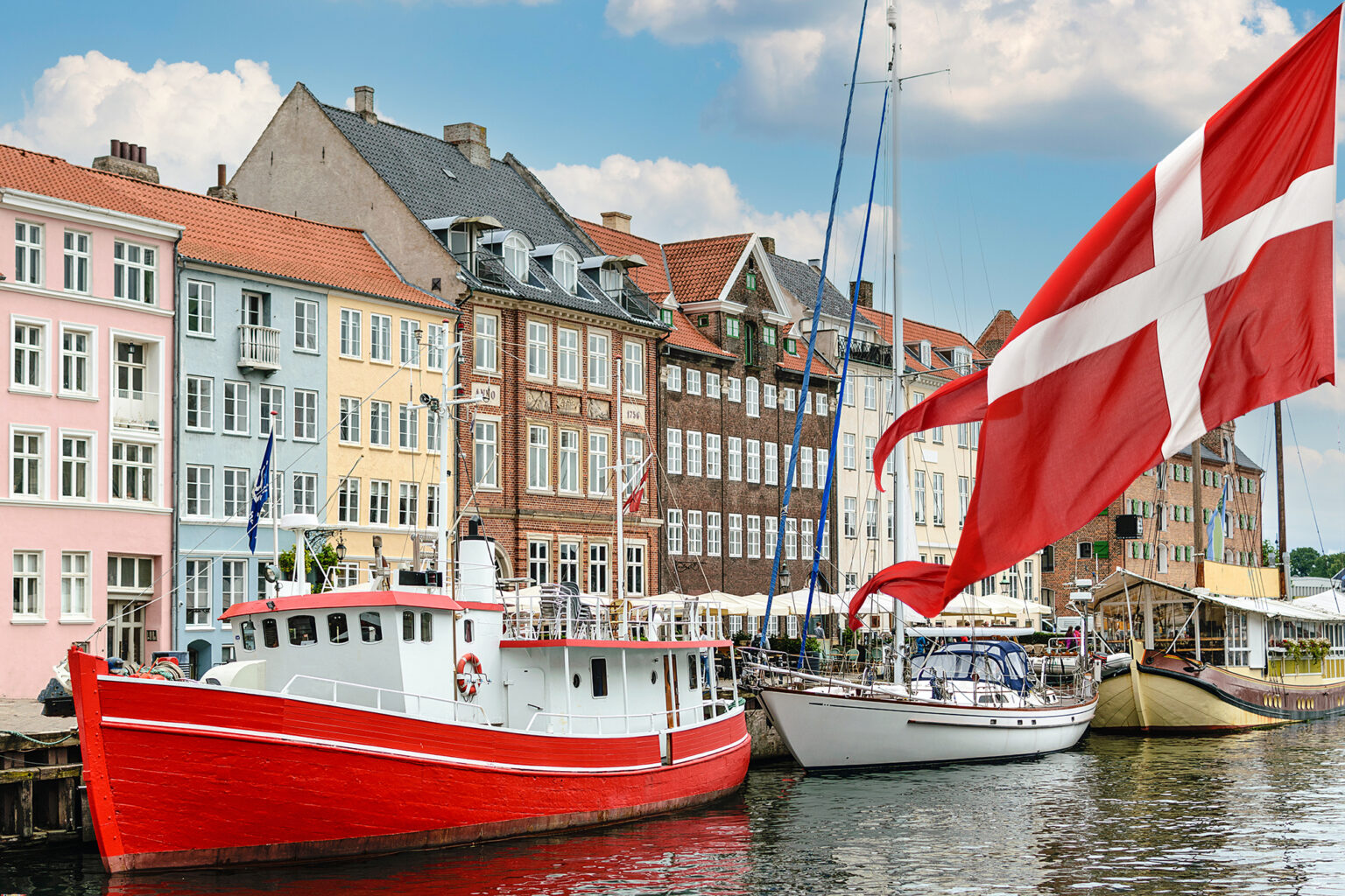 harbour in Copenhagen with typical colorful houses and boats with national flag of Denmark