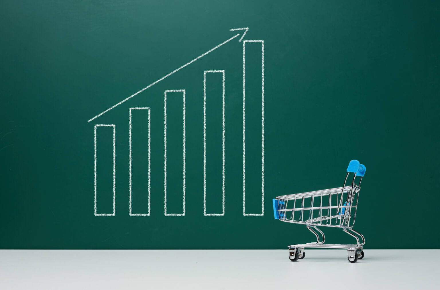 Miniature cart and chalk-drawn graph on green board, price rise concept. High return on sales, inflation