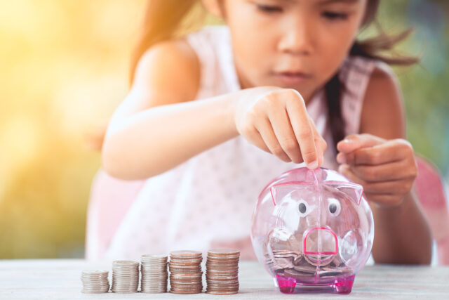 Cute asian little child girl making stacks of coins and putting money into piggy bank to save money for the future