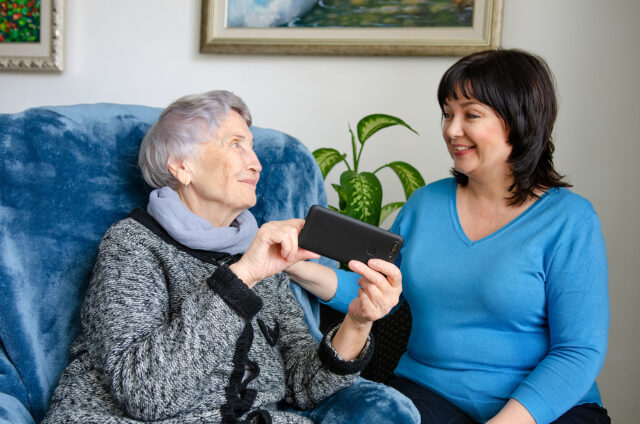 Cheerful female caregiver teaching an elderly woman how to use a