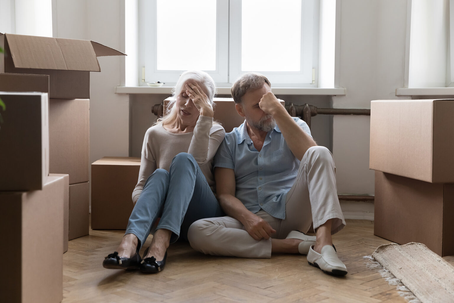 Older couple looking exhausted sitting next to moving boxes