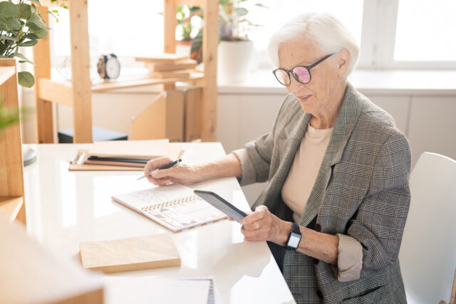 Older woman working at a desk looking at a cellphone