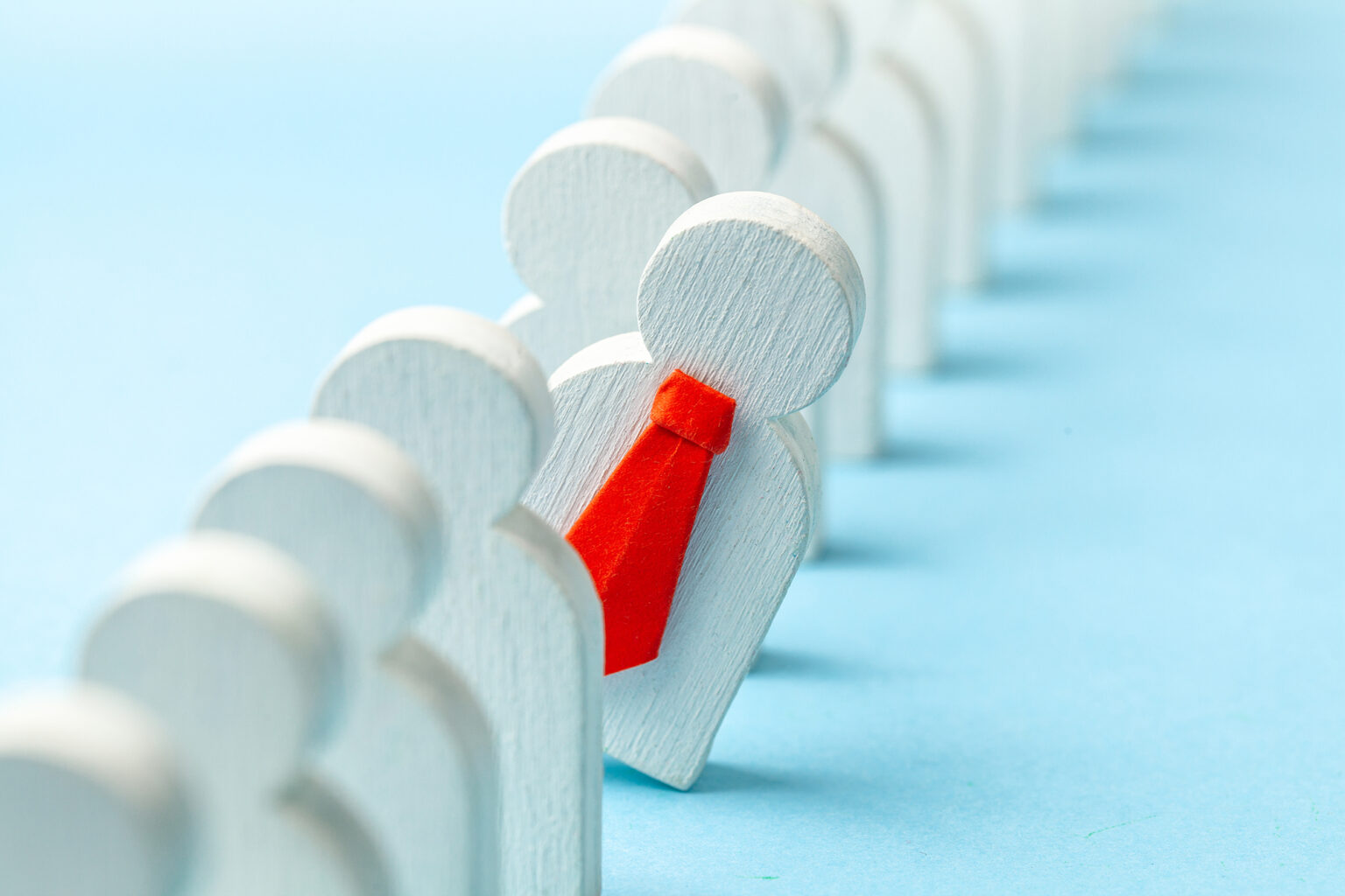 Row of wooden figures with one leaning out wearing a red tie