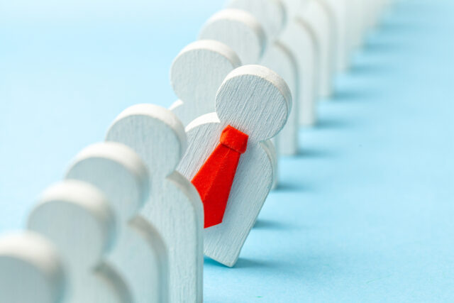 Row of wooden figures with one leaning out wearing a red tie