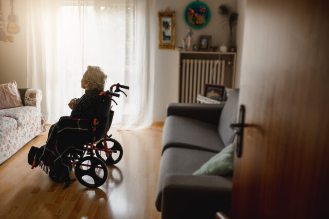 Old sick woman in wheelchair in the middle of domestic room alone
