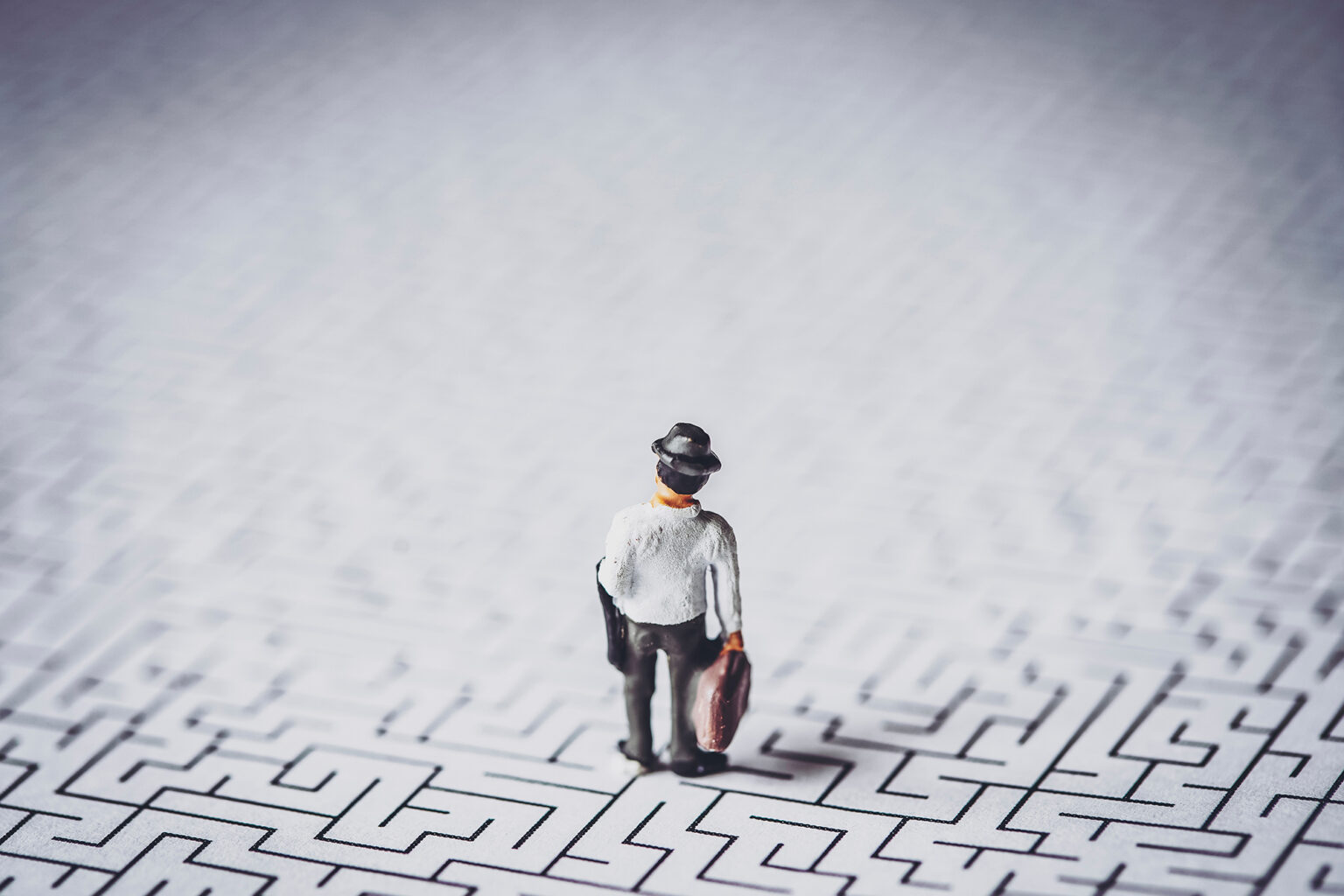 Back view of a minature worker holding a brief case standing on a maze