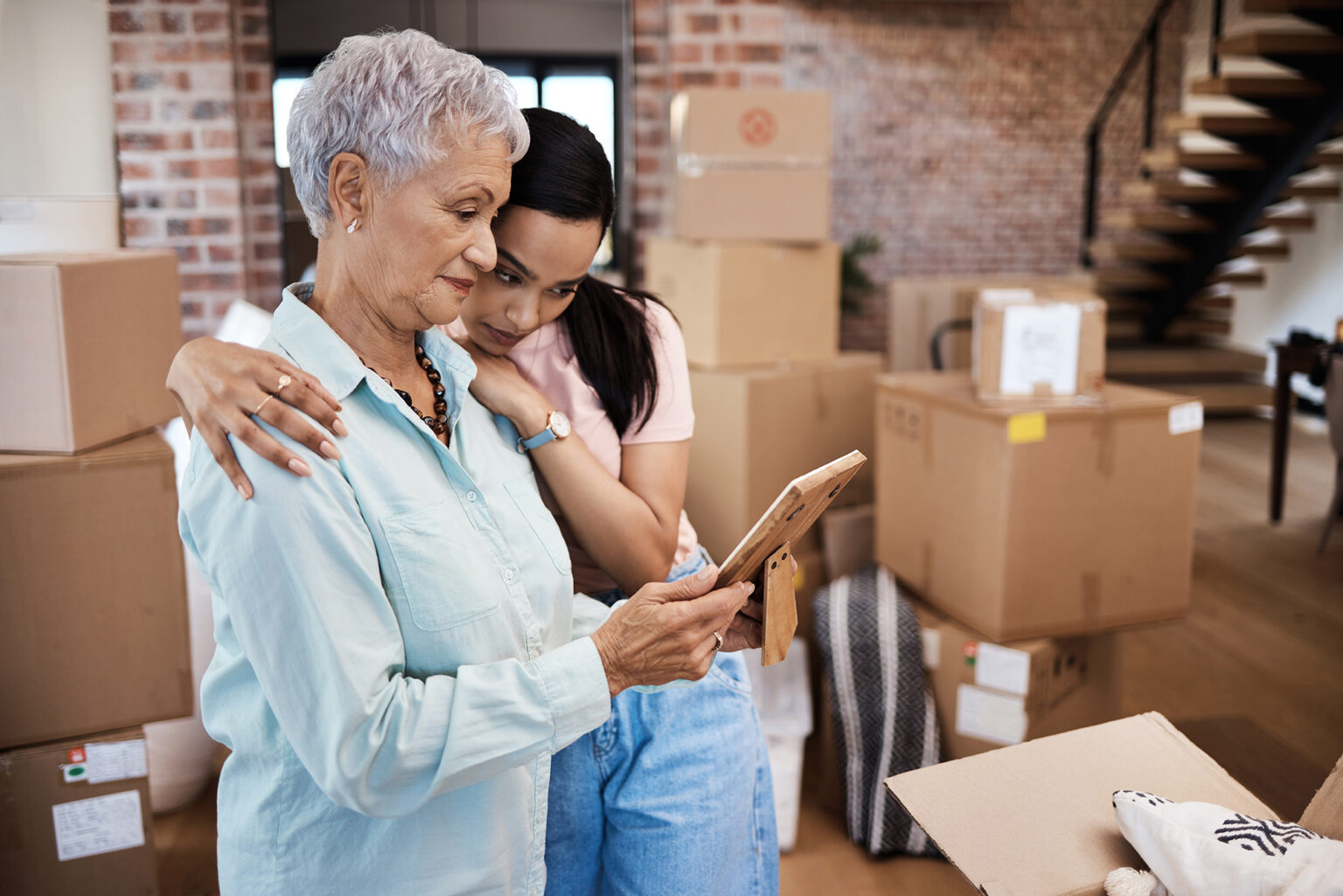 senior woman looking at a photograph with her daughter while packing boxes on moving day