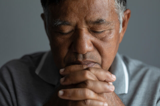 Close up of a man's face holding his hands together with his eye's closed