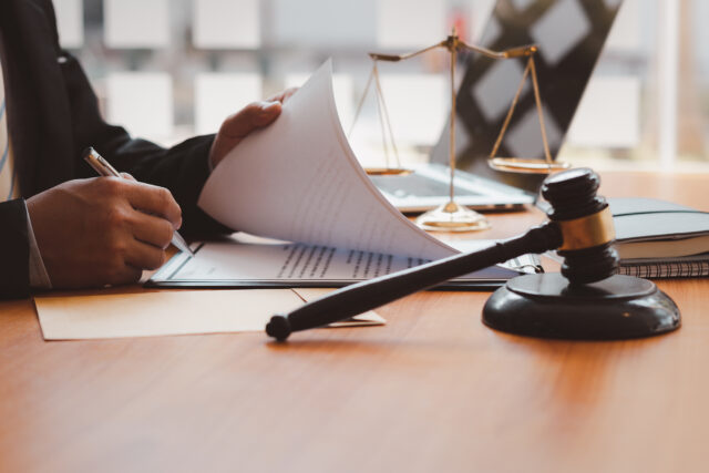 Close up view of hands signing documents on a table with a judge gavel and scales of justice