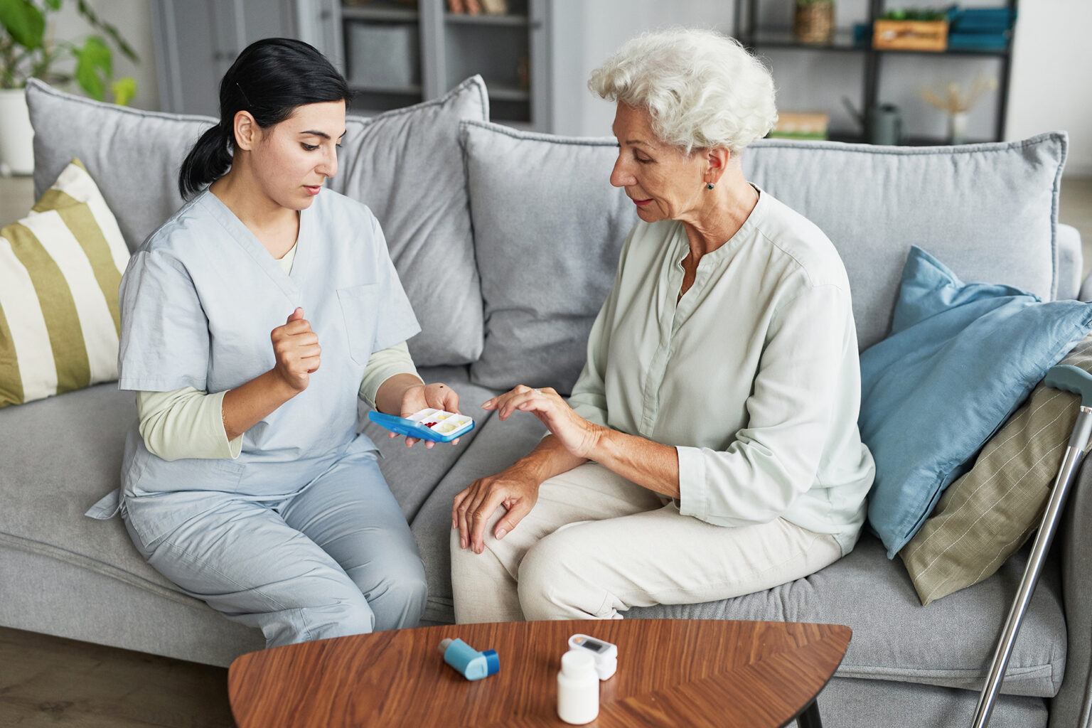 Portrait of a young nurse showing pill box to a senior woman sitting on a couch at home
