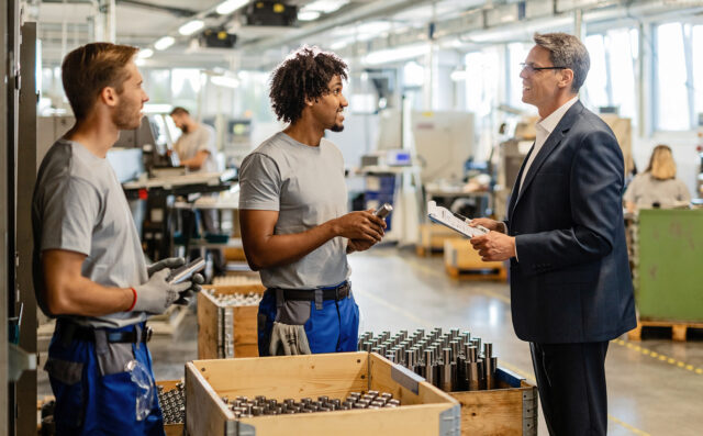 Happy businessman talking with metal workers while visiting the production facility