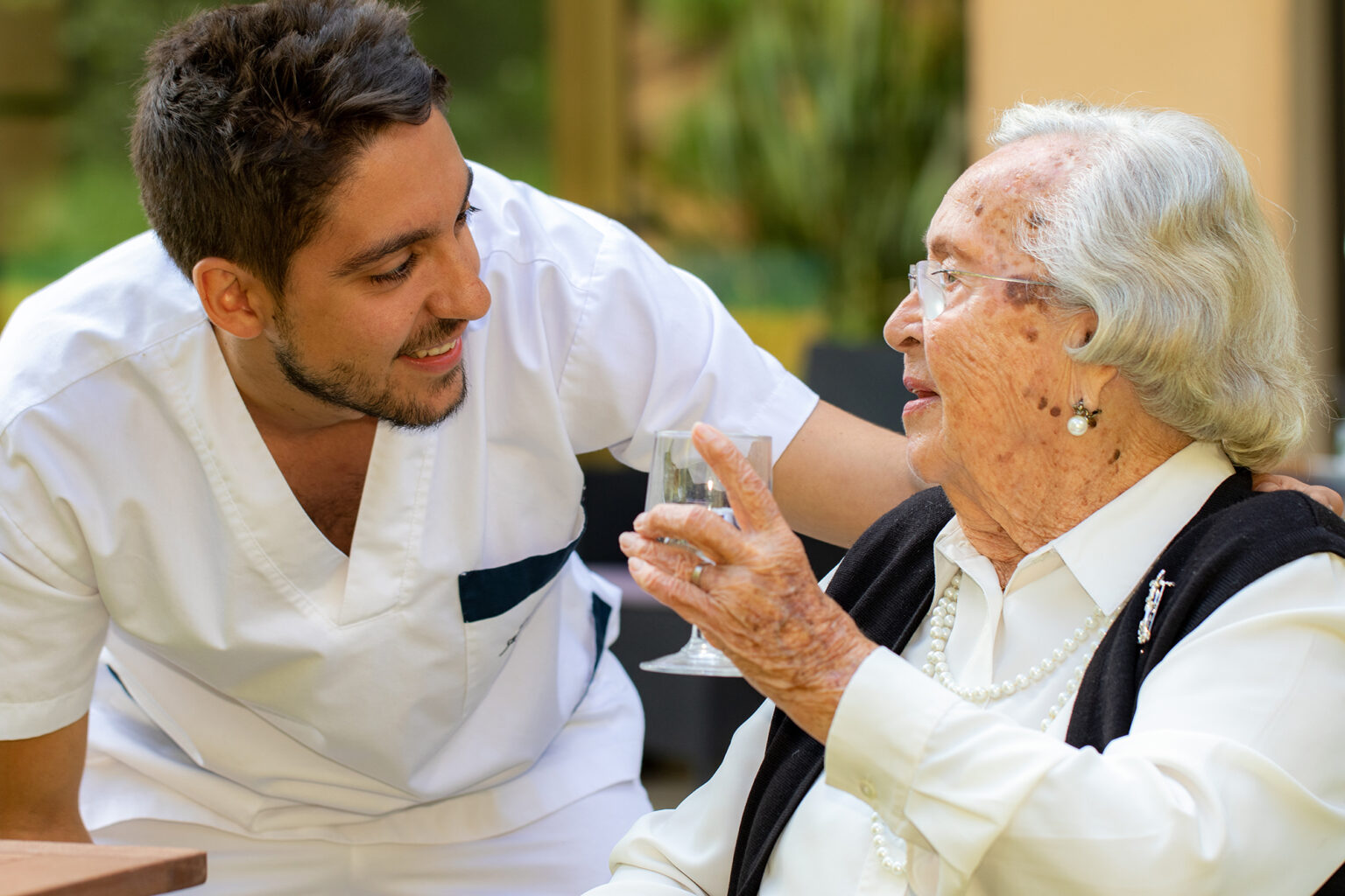 Older woman holding a glass and talking to a young home health aid