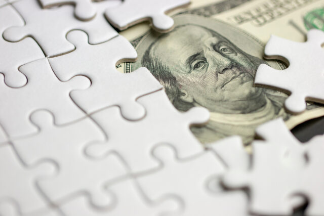 Dollar bill beneath a white jigsaw puzzle