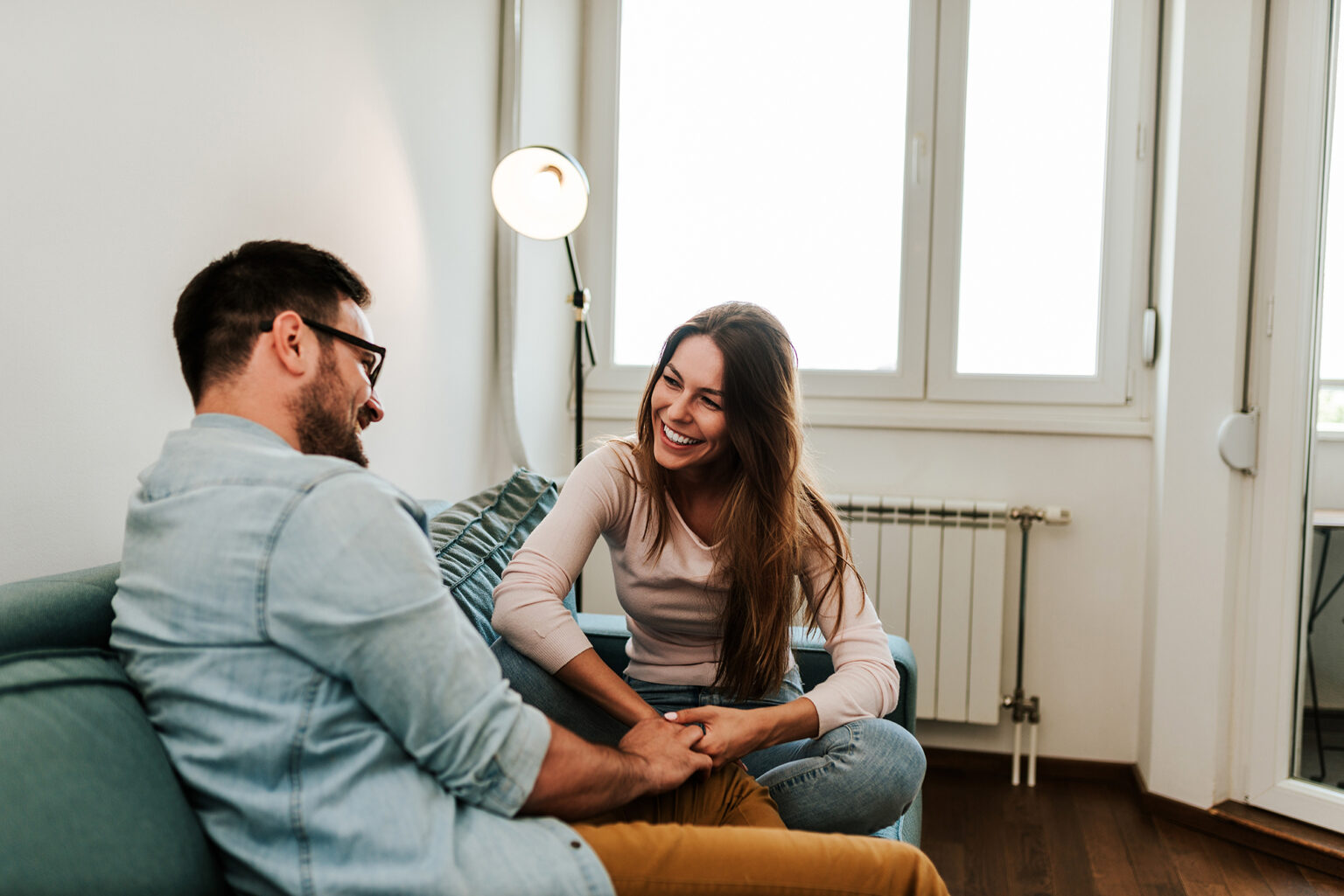 couple holding hands while talking on sofa