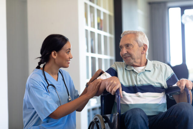 Female nurse looking at elderly man in wheelchair and smiling