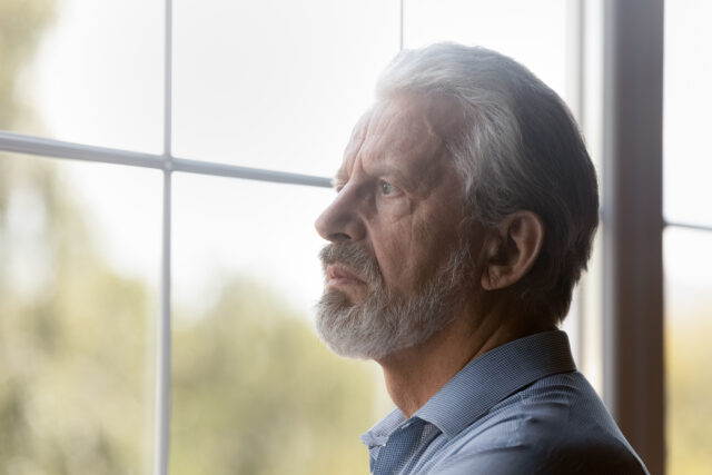 Older man looking contemplative out a window